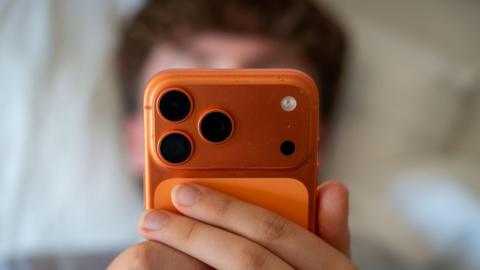 A teenage boy is pictured staring into a phone, suggesting he is using social media.