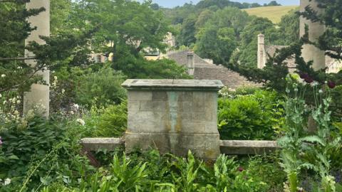An empty plinth in a lush, green garden where a statue once stood