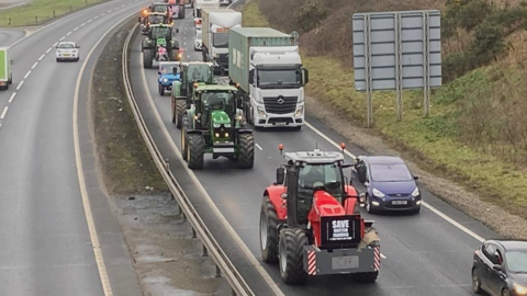 Tractors are pictured heading down one of the lanes of the A14. Other vehicles drive past them in the parallel lane.