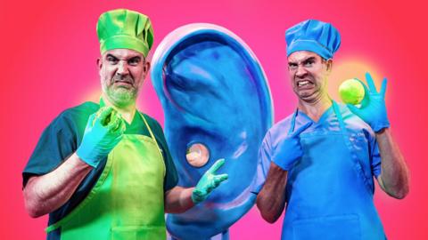 Doctors Chris and Xand wearing chef hats and aprons, with a big blue ear model inbetween them
