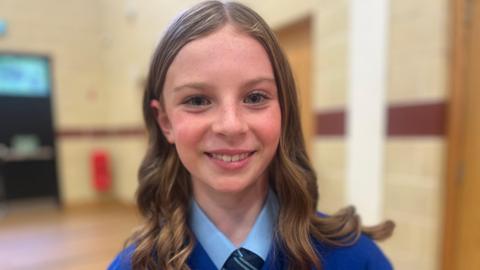 Caoimhe is smiling. Her hair is styled in curls. She's wearing a blue uniform.