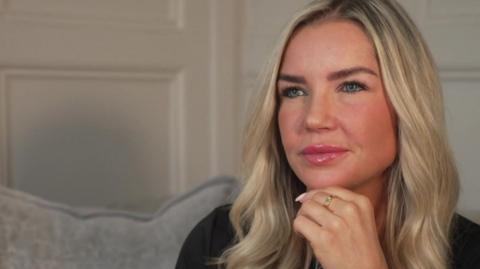 Mum Stephanie Wilkinson with long blond hair and blue eyes. She is sitting on a grey sofa and her hand is resting on her chin.