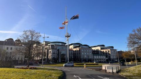 A roundabout with large flag poles in the middle and office buildings behind