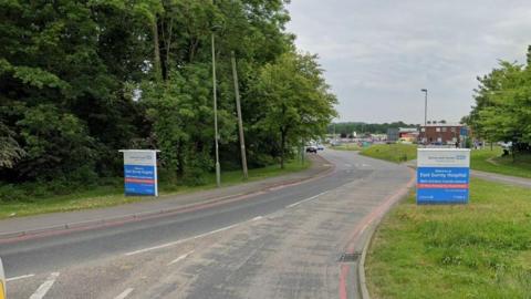 The road leading in to East Surrey Hospital with blue signs and the name of the hospital on the side of the road