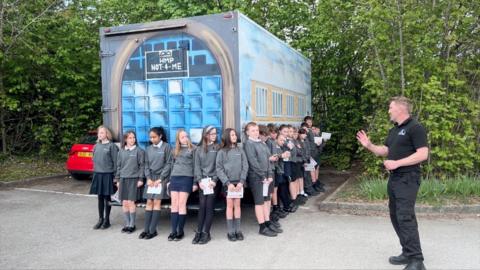 School children stood around a van converted into a 'prison' cell
