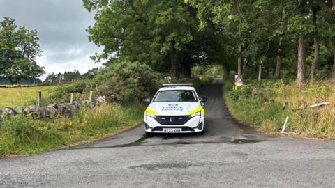 A police car parked on a wooded lane