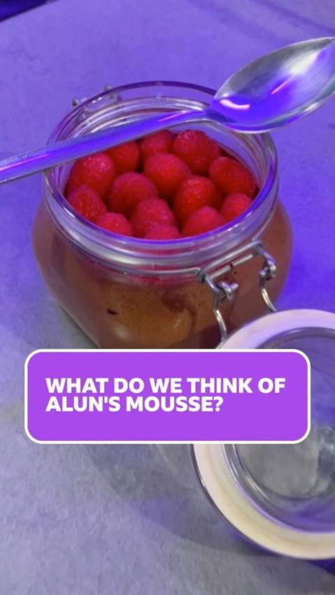 A picture of a glass kilner jar with chocolate mousse inside and raspberries on the top, with a silver spoon across it.