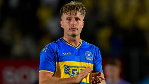 Jodan Dyer head and torso shot, wearing Torquay's away kit of blue and yellow, as he claps supporters 