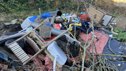 A generic shot showing a pile of waste including chairs, plastic crates, road signs, bins and garden waste.