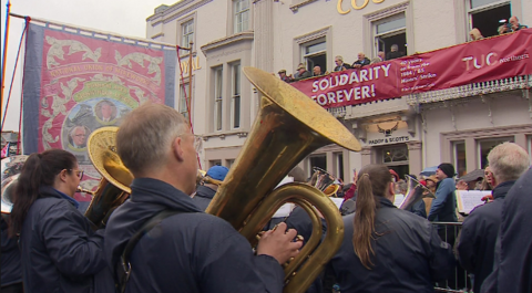 A brass band playing in front of a banner saying Solidarity Forever, hung from a hotel balcony