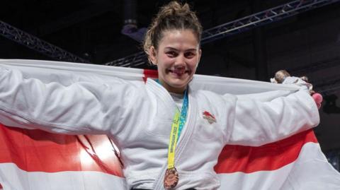 Jemima Yeats Brown with bronze medal around her neck, holding an England flag up behind her