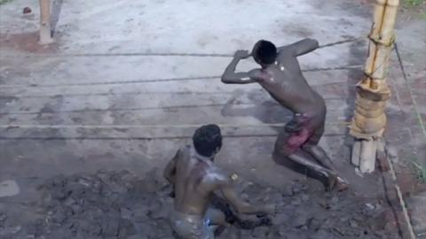 Two people covered in mud move around a wrestling ring