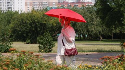 Woman carrying umbrella to offer shade through park during heatwave.
