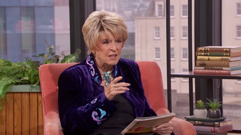 Rip Off Britain's Gloria Hunniford sitting on an orange velvet chair in the Morning Live studio in a purple jacket. She is wearing a necklace and has blonde short hair.