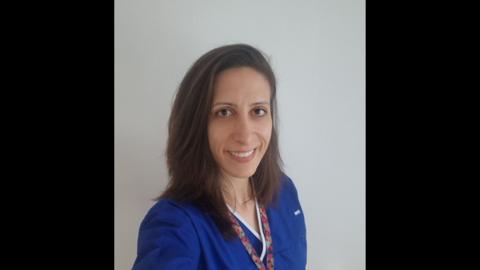 A woman with brown hair and wearing a blue NHS uniform. 