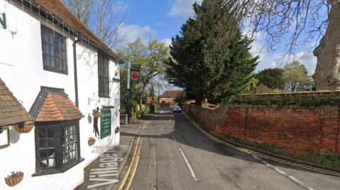 Village Road on streetview, showing a white pub, a narrow road and a red brick wall