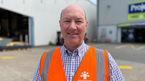 John Bampkin wearing a blue, red and white lined shirt with an orange hi-vis vest on