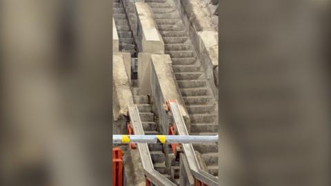 Concrete stairs can be seen beneath escalators at a Tube station.