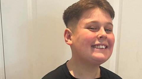 Mason has brown hair and is smiling while wearing a black T-shirt.