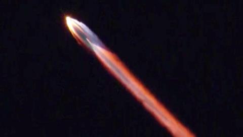 A multicoloured stream of light emanates from a rocket in the night sky.