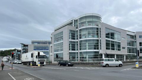 Dorey Court, in Admiral Park, Guernsey, home to many finance companies. Dorey Court is a modern, multi-story office building with extensive glass windows and a rounded corner. 