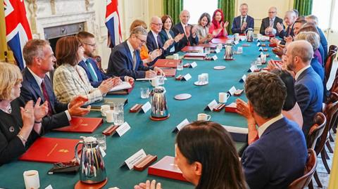 Cabinet members applaud Starmer as he holds pen during first cabinet meeting