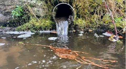 Liquid pouring from an open pipe into a river 