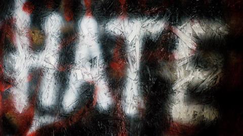 The word Hate in white spray paint written on a wall.