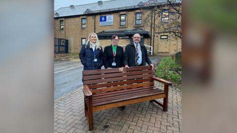 Two women, police business manager Katy and councillor Susan Bellamy, and one man, councillor Martin Morrell, stand behind a bench outside Wombwell Police Station.
