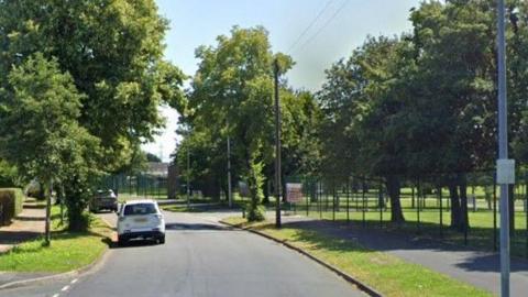 A section of Bracknell Avenue close to the junction with Kirkby High School. The school entrance can be seen on the right hand side. The road is lined with a number of trees.