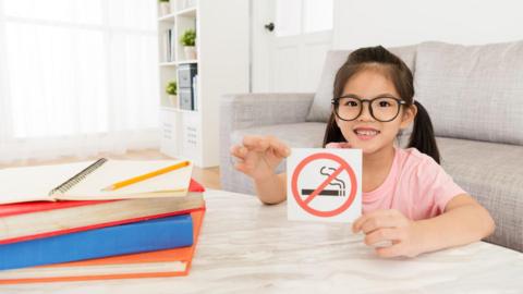 Little girl looking at camera presenting no smoking notice.