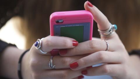 Female hands with rings and red nails hold a pink smartphone