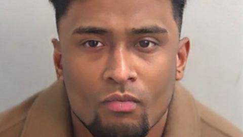 Mug shot of Junead Ahmed, he has a groomed, dark chin beard and dark short hair. He is wearing a caramel wool coat, the top of which can be seen in the image