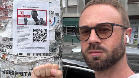 A photo of Andrei Gnyot clenching his fist in a solidarity symbol and next to a poster reading 'free Andrei Gnyot' 