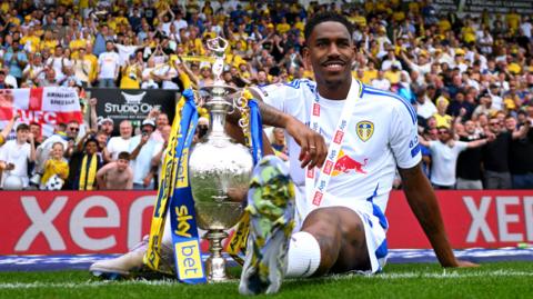 Junior Firpo poses while sat on the pitch with the Championship trophy