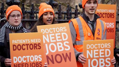 BMA resident doctors hold placards reading 'doctors need jobs now' while striking in London in December