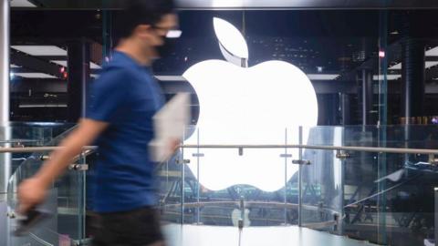 An Apple employee walking past an Apple logo