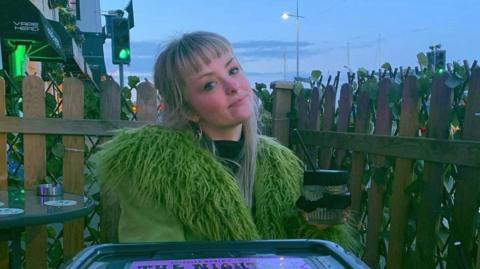 A woman wearing a green jacket, sitting outside.
