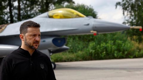 President Volodymyr Zelenskiy speaks to the media in a front of an F-16 fighting aircraft 