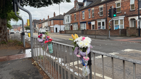 Three bunches of flowers tied to railings at a pedestrian crossing.