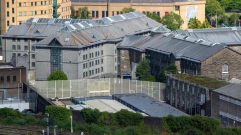 A grey, large building surrounded by trees and other buildings