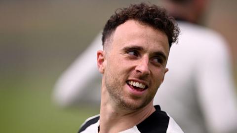 A photo of Diogo Jota smiling while looking to the right. He is wearing a white shirt. 