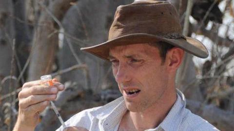 Professor Alan Wilson is extracting fluid from a small pot into a needle. He looks focused and is wearing a shirt and hat.