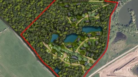 An aerial map of the proposed development which has a red boundary outlining the land. In the middle there are four lakes surrounded by trees. The roofs of lodges and caravans can also be seen. Sand is visible to the right of the development.