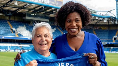 Barbara Charone and Brenda Edwards celebrate the donation at Stamford Bridge