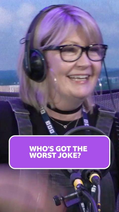 Justine Field is laughing the studio she has short blonde hair with black framed glasses 