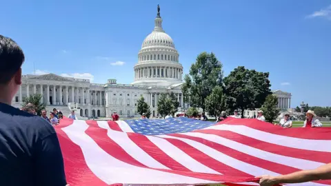 Americans hold up a large US flag as they walk on the lawn just outside Capitol Hill