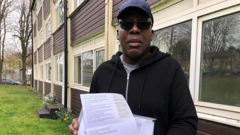 A close up of Joseph, wearing a blue baseball cap and sunglasses, standing outside the block of flats in Luton that is in need of fire safety work. His quarterly service and sinking fund bill is set to increase by more than 300% from April