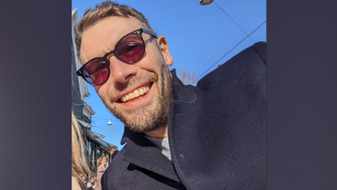 Aran Potkin from Farnham. Aran is wearing sunglasses and has fair hair and a short beard. He is wearing a navy coat.