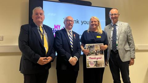 William Mulroe BEM stood with staff from Mid Yorkshire Teaching NHS Trust, with one woman holding up a thank you card.